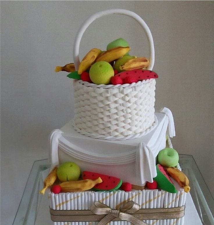 Layered cake with a white fruit basket filled with fruits at the top